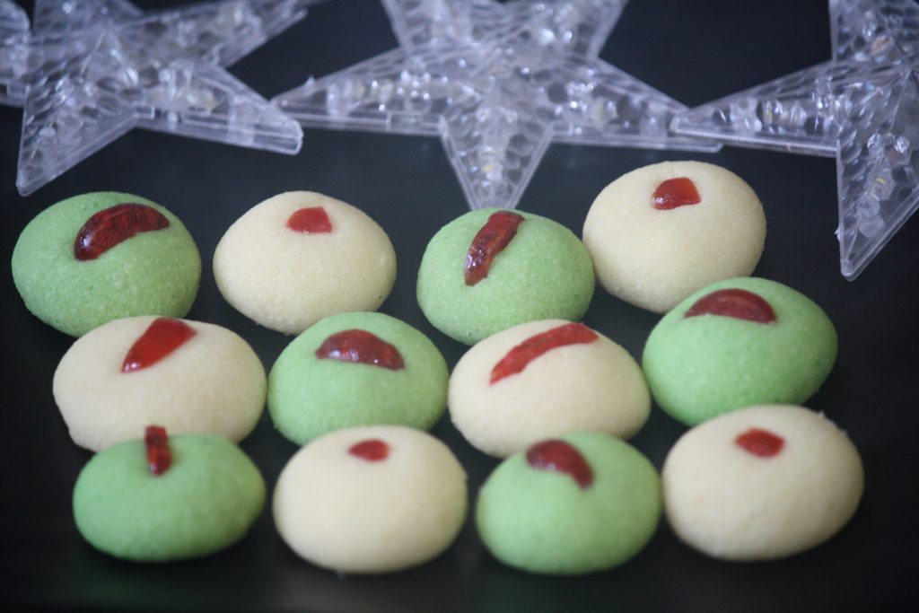 White and green nankhatai topped with cherries on a black tray with stars.