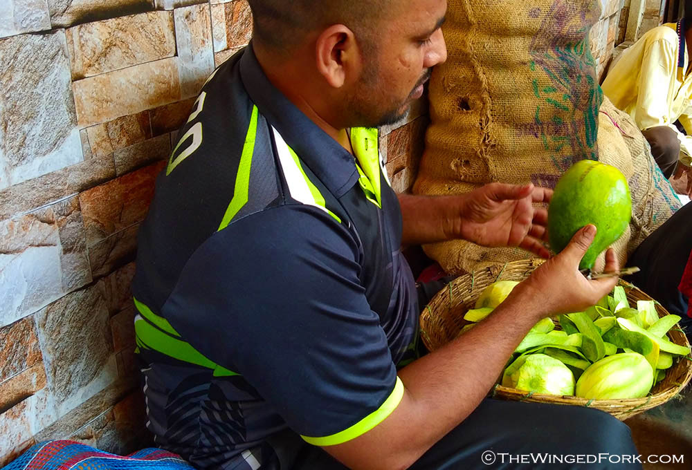 Market vendor peeling the skin of raw green mangoes.