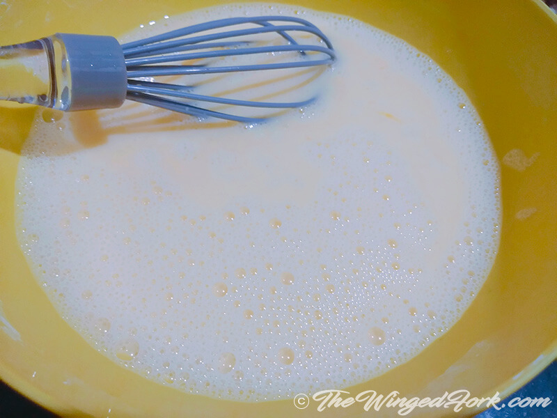 Yellow bowl of eggs beaten to a froth with a whisk in it
