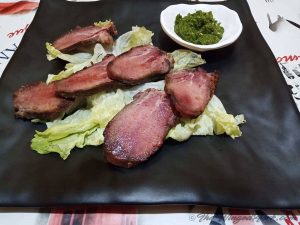 Corned tongue slices on a bed of lettuce with a bowl of green chutney.