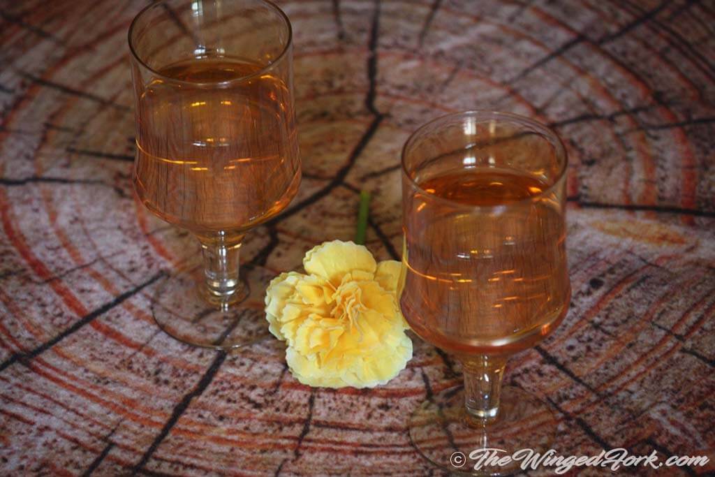 Homemade pineapple wine in two glasses next to a yellow flower - Pic by Abby from AbbysPlate