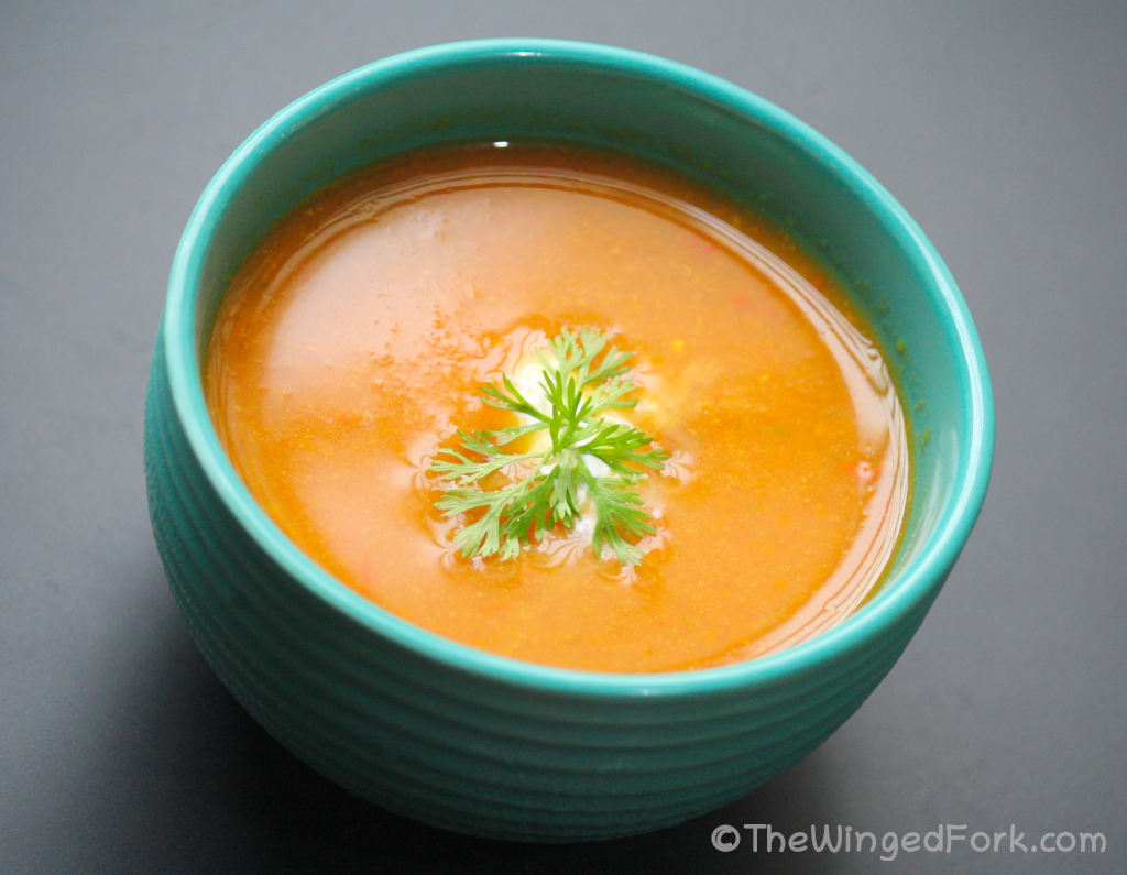Side view of tomato soup in a blue bowl topped with coriander (cilantro) and cream
