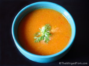 Tomato and carrot soup in a blue bowl on a black table topped with cream and fresh coriander