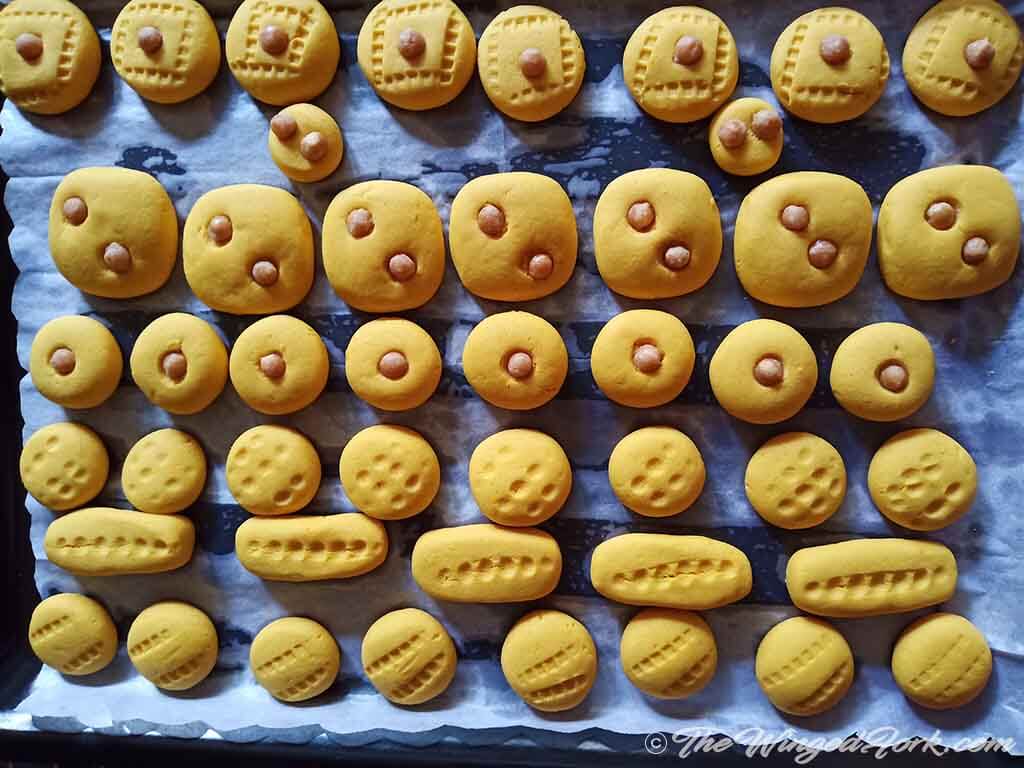 Yellow colored custard powder cookies are cooling on a baking tray.
