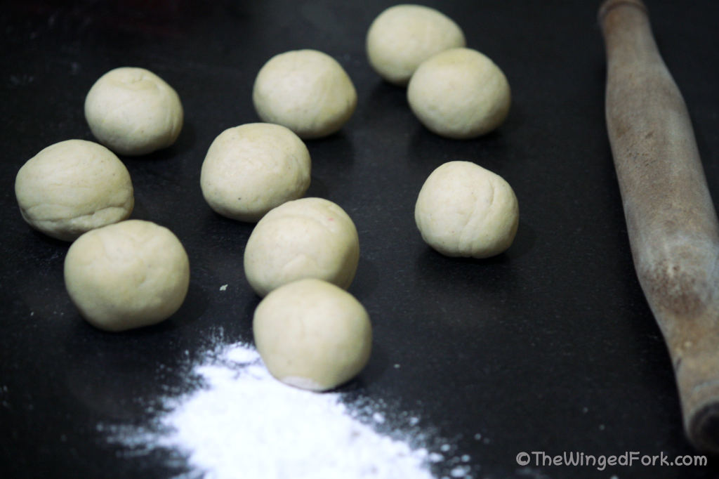 Small dough balls, a rolling pin and a handful of dough on a black surface.
