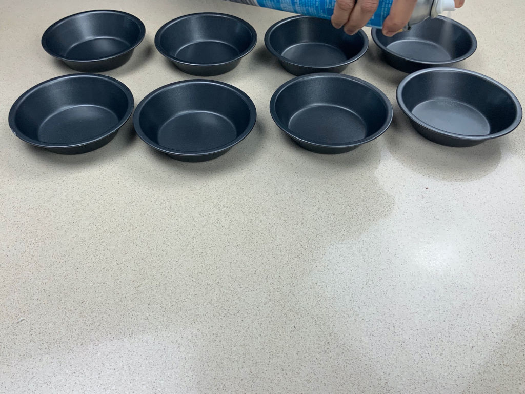 8 pie tins in 2 rows on a cream surface