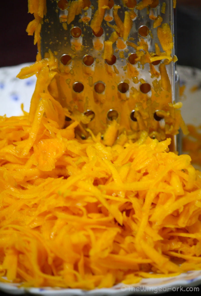Grated red pumpkin on a white plate and a steel grater.