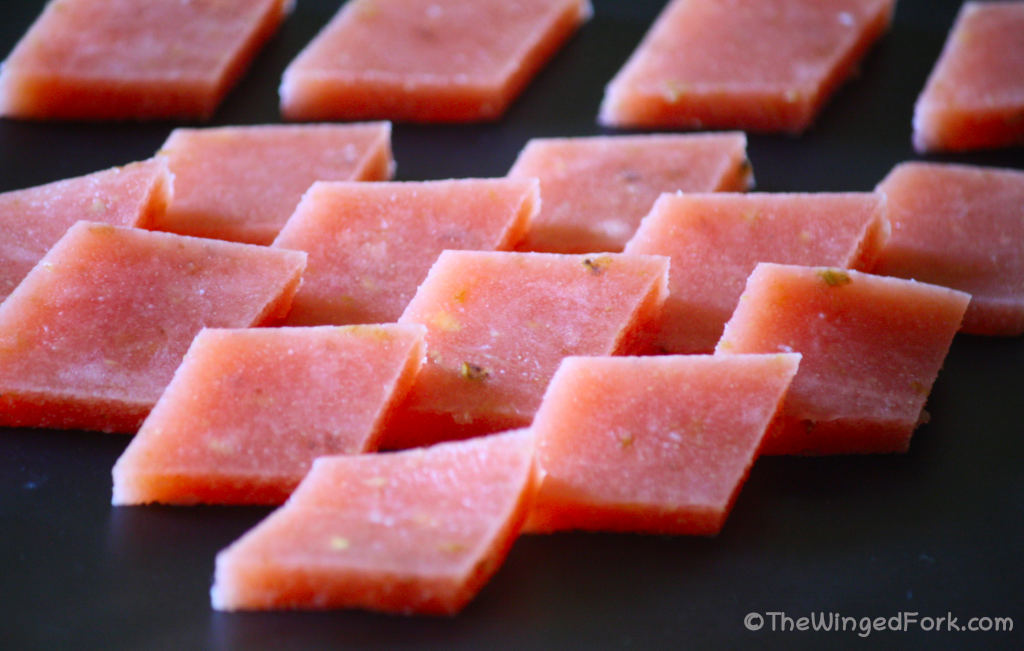 Pink slices of guava cheese on a black tray.