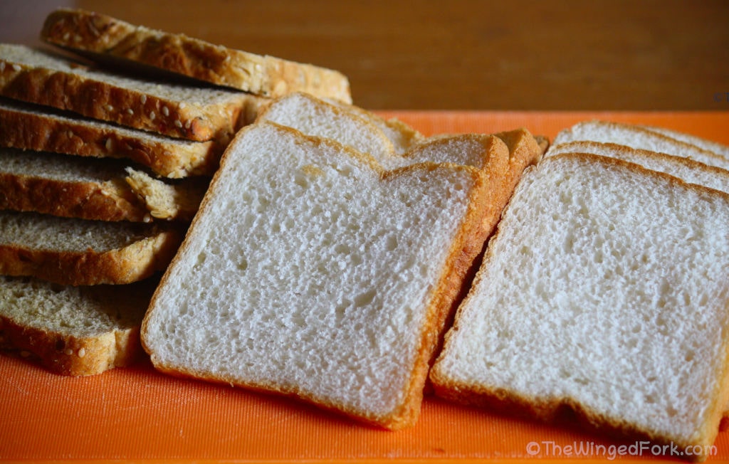 White and brown bread slices on a orange cutting board.