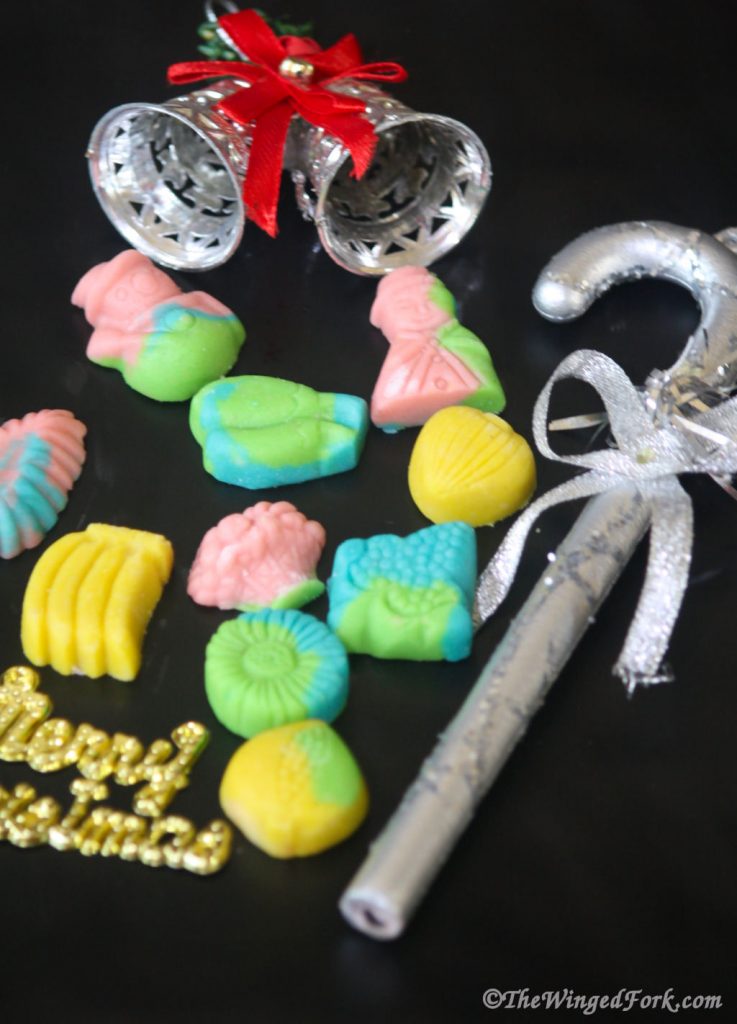 Colourful marzipan shapes on a black plate with Christmas bells and cane.