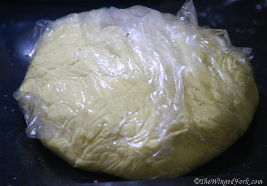 Dough in plastic wrap on a black surface.