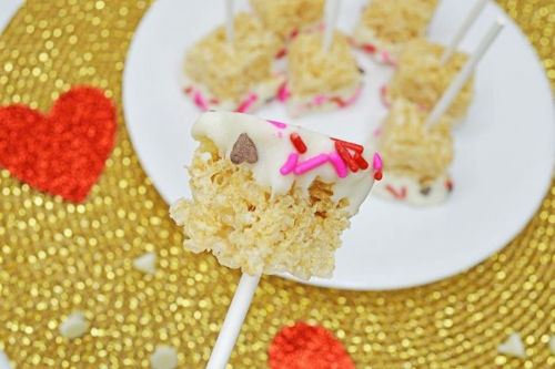 A few krispy rice pops served on a white plate next to red hearts.