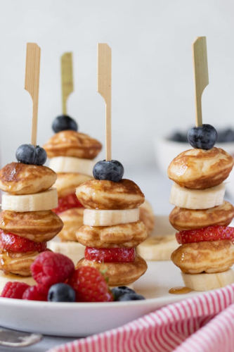 Mini pancakes on a stick between banana and strawberry slices and blueberries.