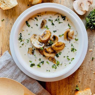 Mushroom soup in a white bowl next to bread.