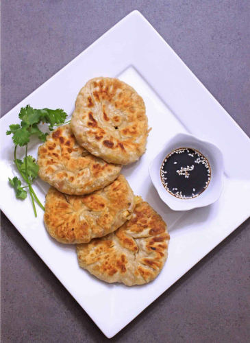 Vegetable stuffed chinese pancakes with soy sauce in a white bowl.