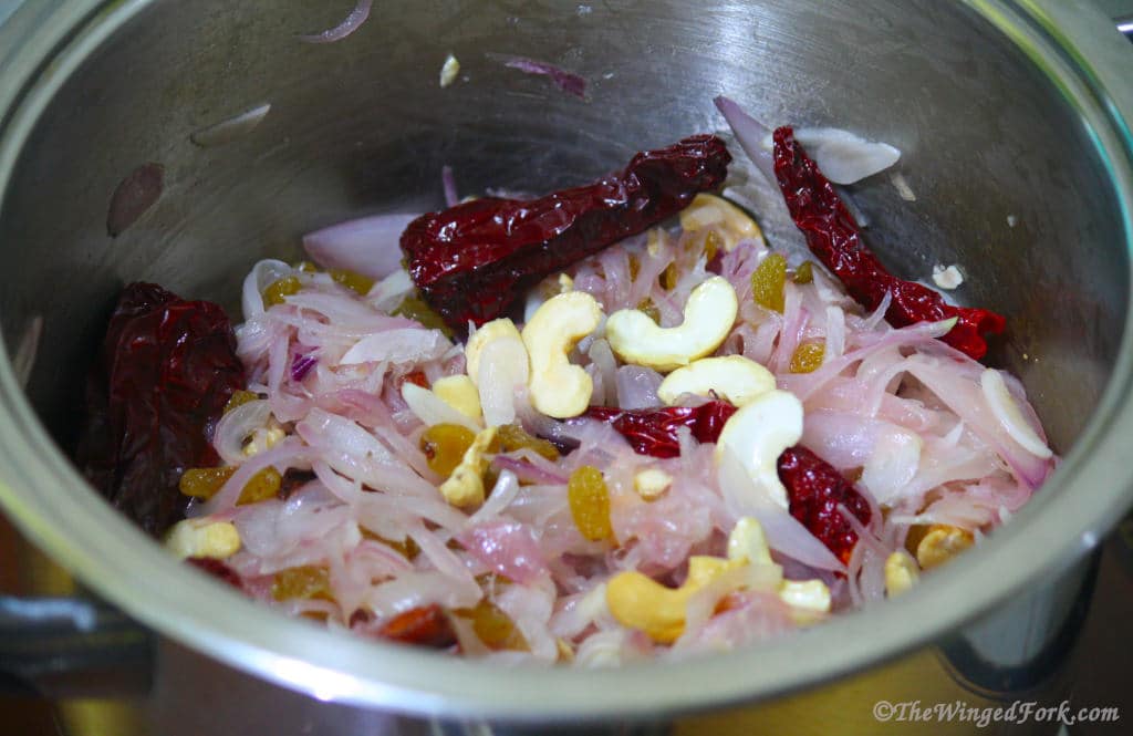 Onions, red chillies, raisins and cashews in a vessel.