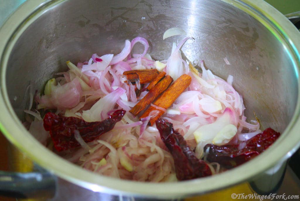 Onions, red chillies and cinnamon sticks in a vessel.