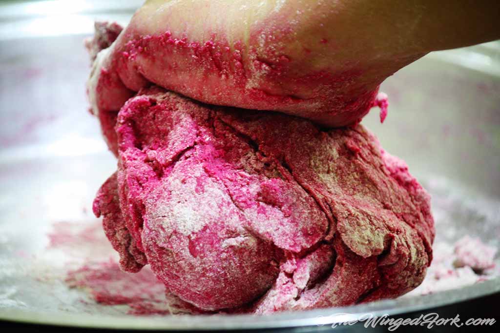 Hand kneading the pink dough in a plate.