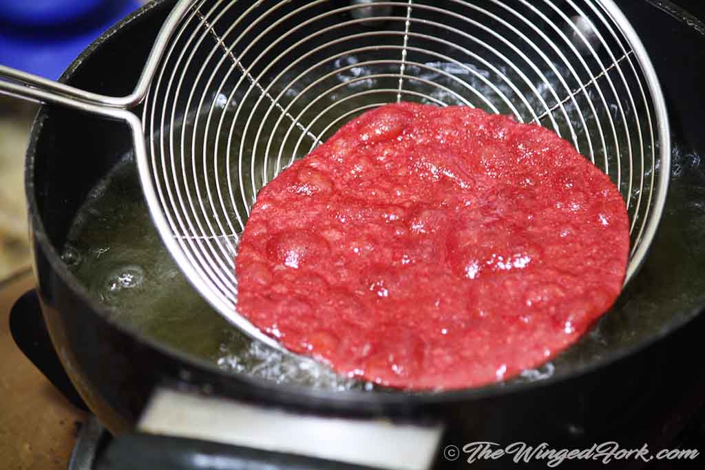 Pink puri fried and drained with a skimmer in the hot oil kadhai.