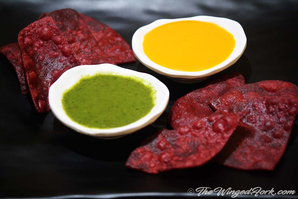 Triangular beetroot puris served on a plate with green chutney and Amras bowl.