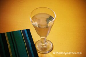 Clear ginger wine in a glass next to a blue book.