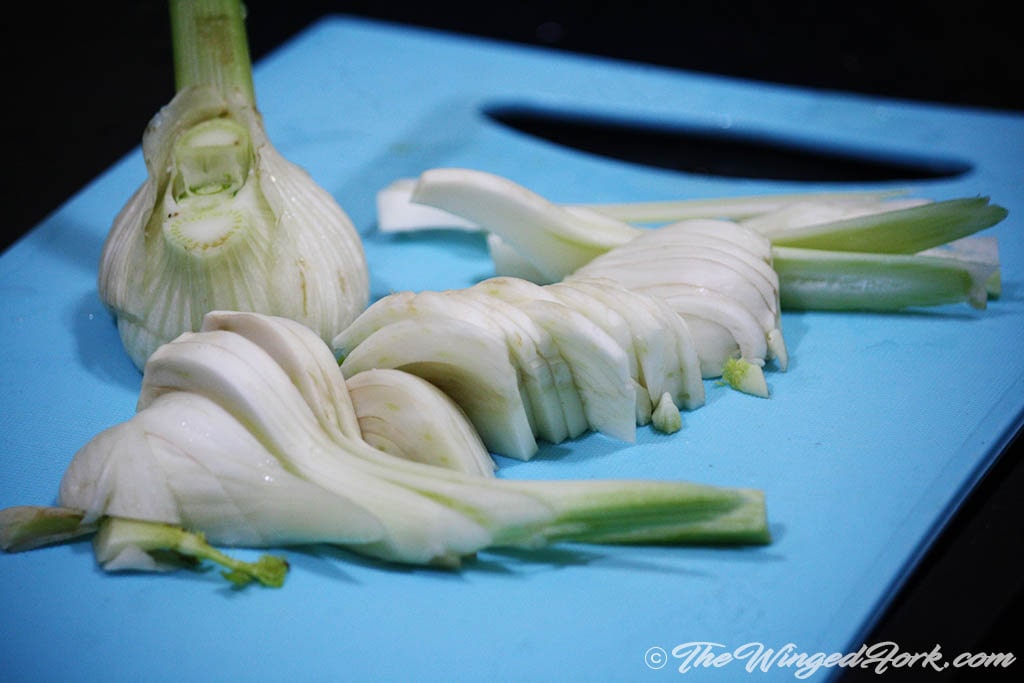 Slices of fennel and whole fennel on a blue cutting board.