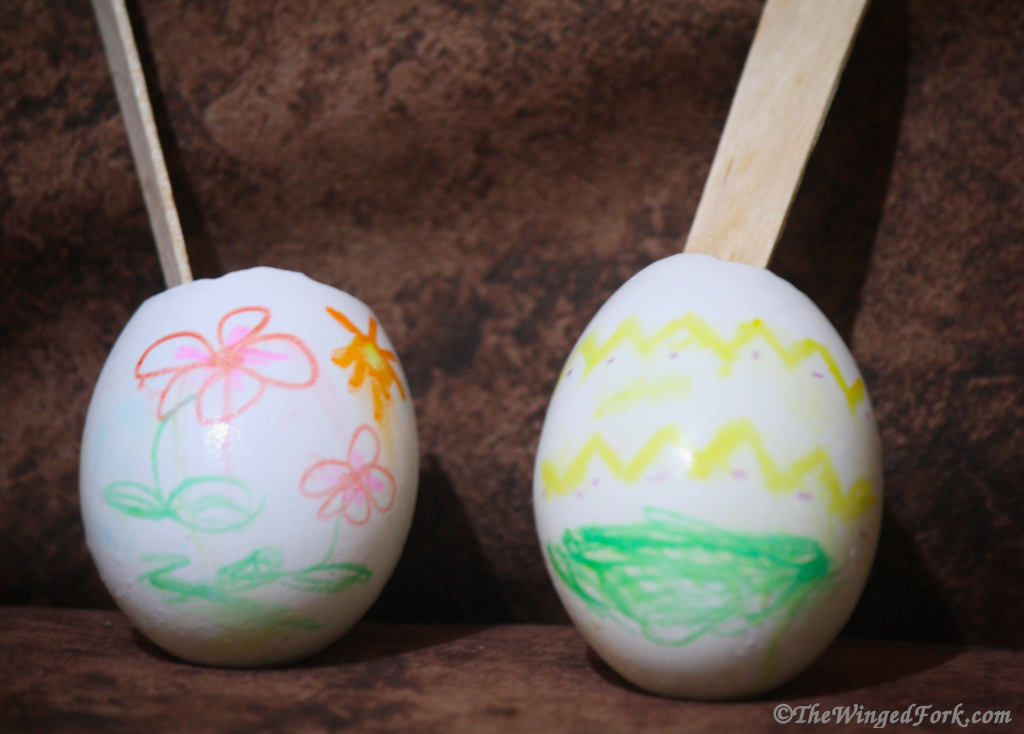 2 decorated Egg shells with wooden spoons in them.