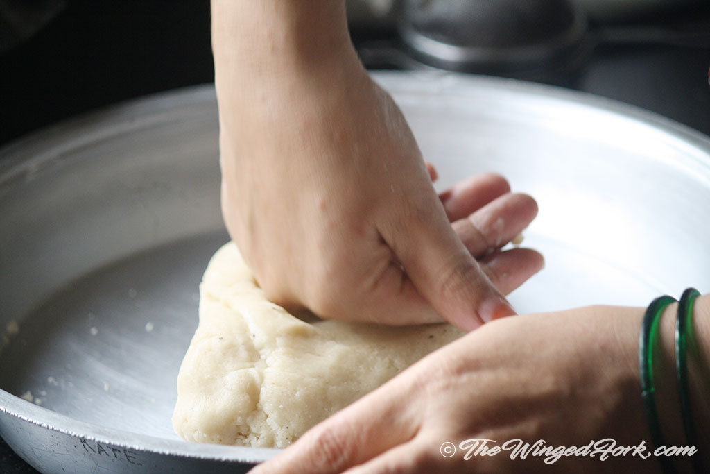 A hand kneading the dough in a thala.