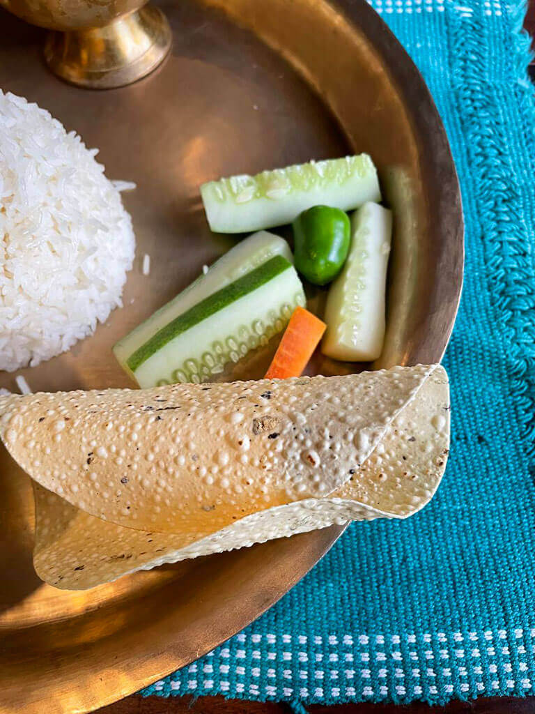 Fried Papad and cut cucumber and carrot in a plate next to rice.