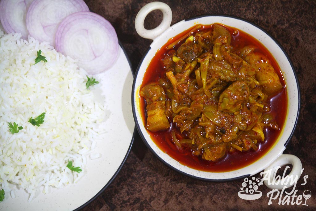 Pork tamriad curry in kadai next to rice and sliced onions in plate.