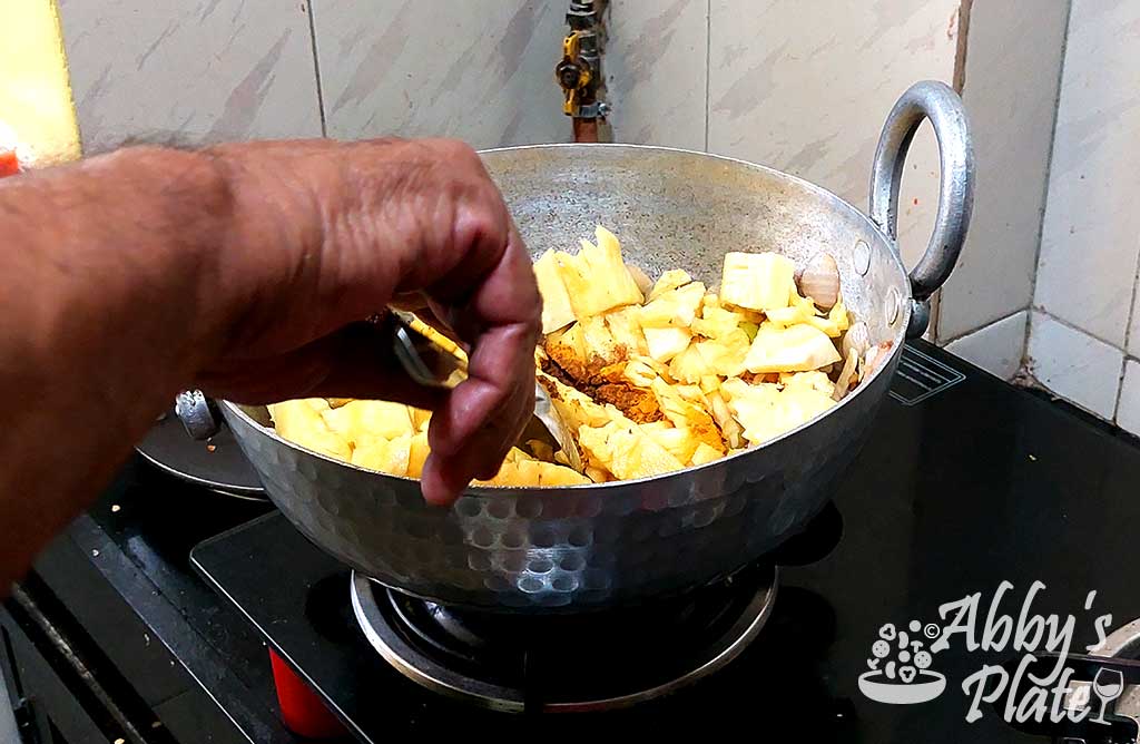 A hand stirring chopped pineapple in a kadai.