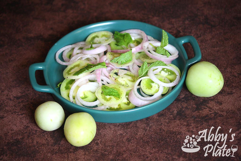 Green tomato salad in a dish with onion rings & mint leaves.
