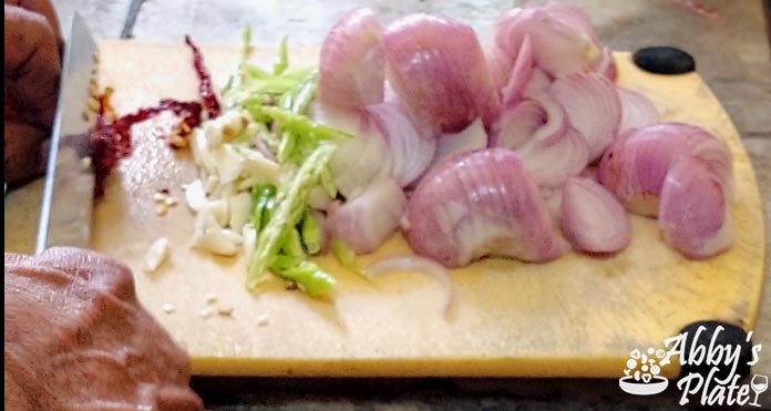 Sliced onions, green chilies, garlic & red chilies on a chopping board.