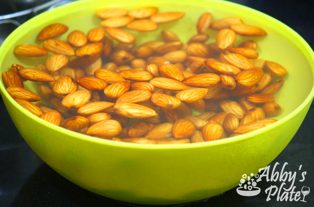 Almonds soaking in water in a yellow bowl.